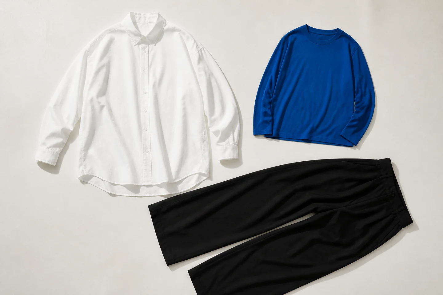 白いシャツ、青い長袖Tシャツ、黒いワイドパンツの三着だけを並べたフラットレイ