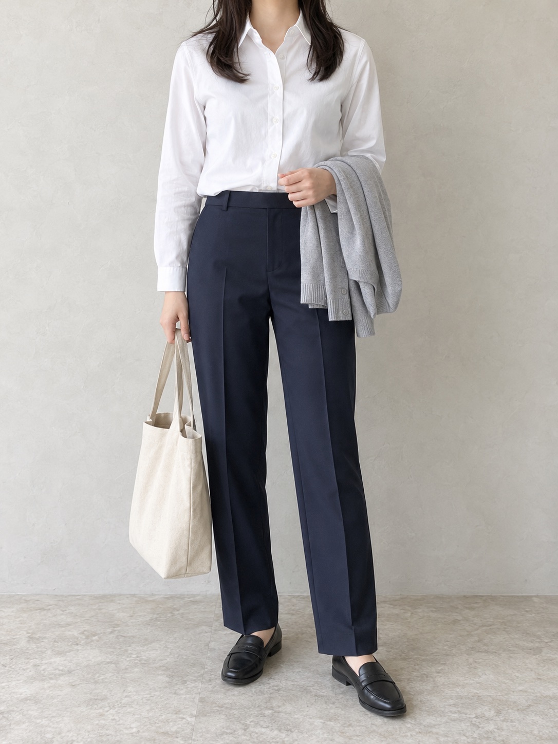 白い長袖シャツと濃紺のパンツ、黒いローファーに、薄いグレーのカーディガンを持った通勤の着こなし例。